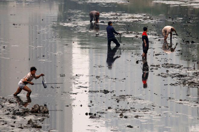 Fishermen walk through the muddy bottom of a polluted canal collecting fish in central Beijing